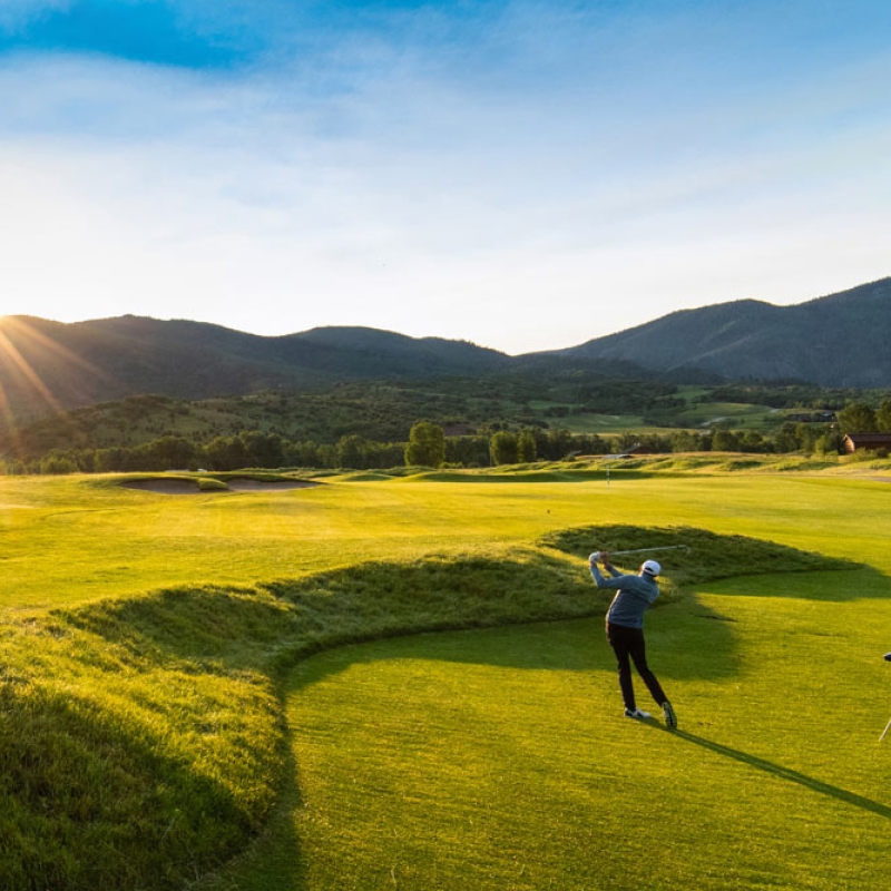 Golfer swinging golf club at sunset
